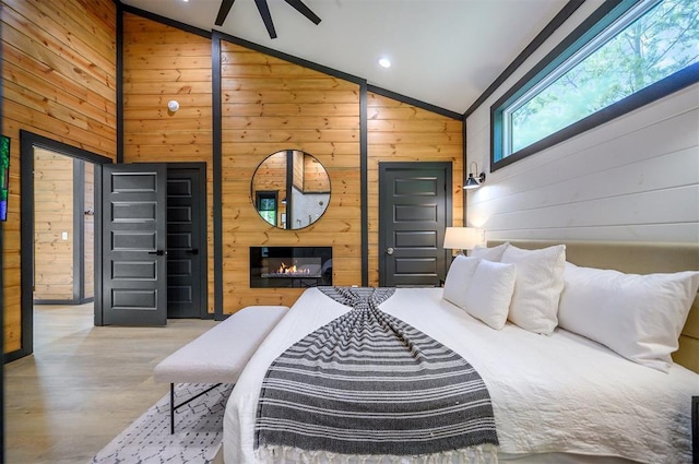 105 S Spruce Trl, Broken Bow, OK 74728 - bedroom featuring vaulted ceiling, wooden walls, wood finished floors, and a glass covered fireplace