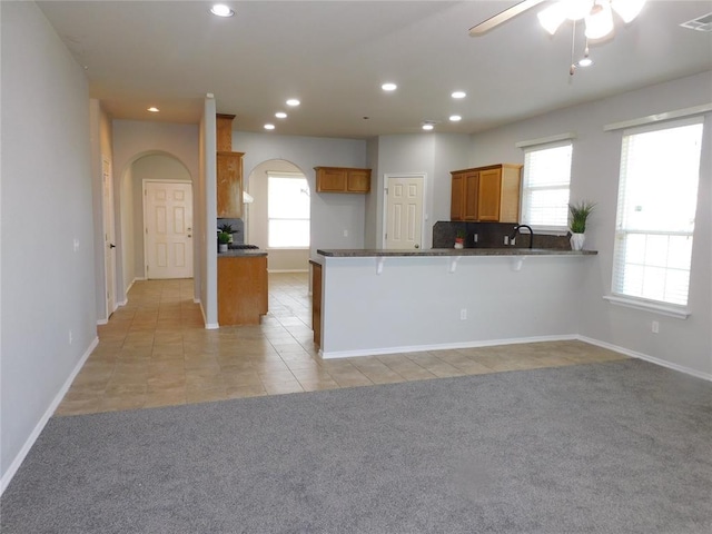 6036 SE 66th St, Oklahoma City, OK 73135 - kitchen with arched walkways, brown cabinetry, a peninsula, light tile patterned floors, and a ceiling fan