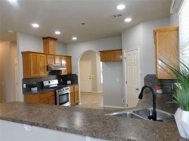 6036 SE 66th St, Oklahoma City, OK 73135 - kitchen featuring gas range, under cabinet range hood, backsplash, dark countertops, and arched walkways