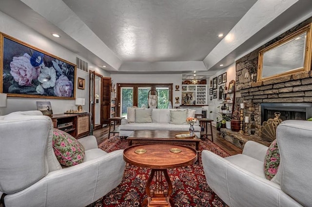 1601 Hazelhurst, Edmond, OK 73013 - living room featuring a raised ceiling, wood finished floors, a stone fireplace, and recessed lighting