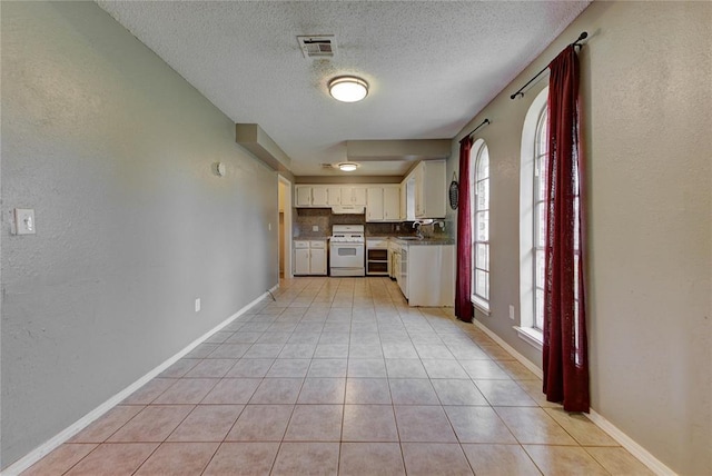 1021 SW 1st St, Moore, OK 73160 - kitchen featuring white stove, a textured ceiling, light tile patterned floors, white cabinetry, and under cabinet range hood