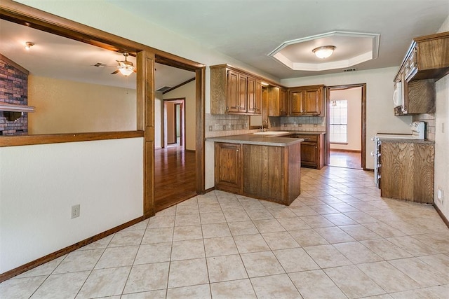 10201 Mantle Ct, Oklahoma City, OK 73162 - kitchen with range, a peninsula, brown cabinetry, decorative backsplash, and ceiling fan