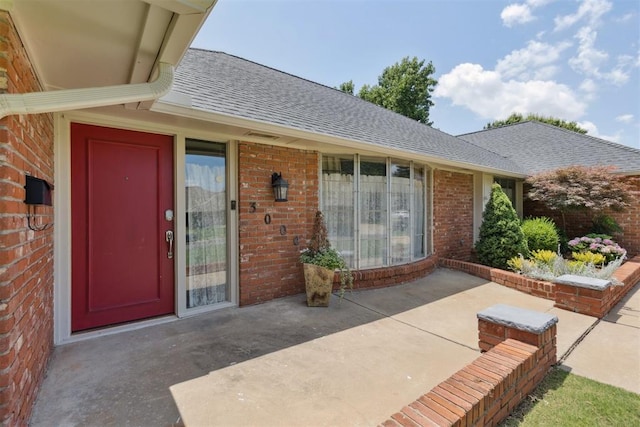 3000 Middlesex Dr, Oklahoma City, OK 73120 - doorway to property featuring a shingled roof, brick siding, and a patio