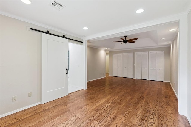 3000 Middlesex Dr, Oklahoma City, OK 73120 - unfurnished bedroom with ornamental molding, a barn door, a raised ceiling, multiple closets, and wood finished floors