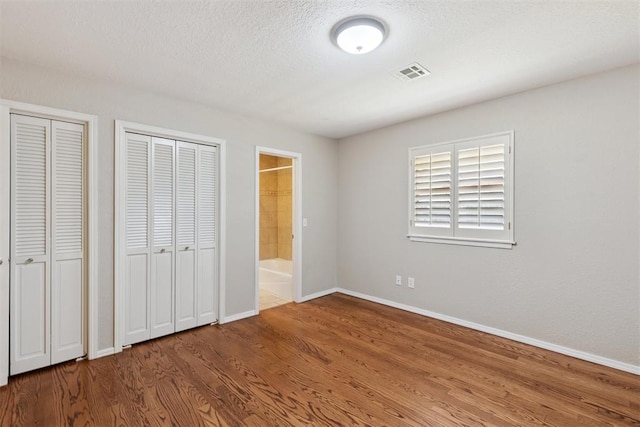 3000 Middlesex Dr, Oklahoma City, OK 73120 - unfurnished bedroom with wood finished floors, multiple closets, ensuite bathroom, and a textured ceiling
