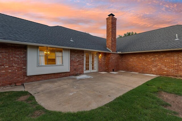 3000 Middlesex Dr, Oklahoma City, OK 73120 - back of house at dusk featuring french doors, brick siding, a chimney, a patio, and roof with shingles