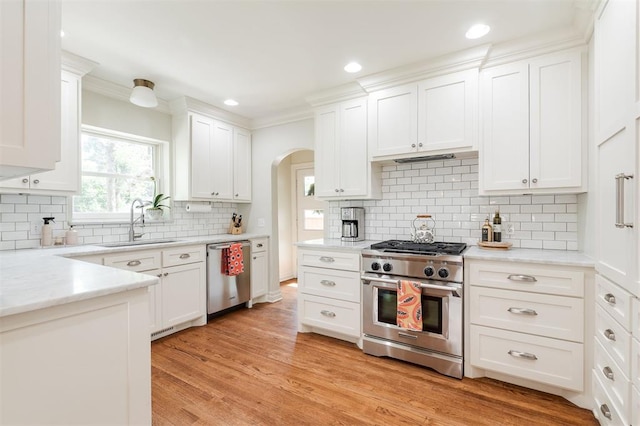 1005 NW 40th St, Oklahoma City, OK 73118 - kitchen with appliances with stainless steel finishes, arched walkways, backsplash, white cabinetry, and light wood-type flooring