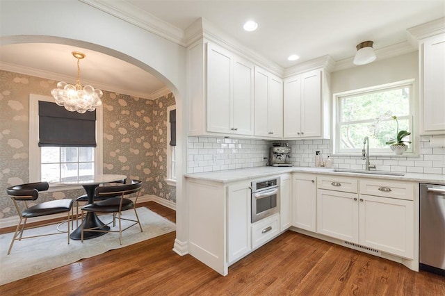 1005 NW 40th St, Oklahoma City, OK 73118 - kitchen with appliances with stainless steel finishes, arched walkways, wood finished floors, ornamental molding, and white cabinetry