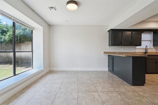 2322 Ripple Creek Ln, Edmond, OK 73012 - kitchen with a textured ceiling, a peninsula, light tile patterned floors, and light stone counters