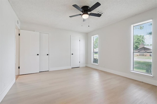 2322 Ripple Creek Ln, Edmond, OK 73012 - unfurnished bedroom with light wood-type flooring, two closets, a textured ceiling, and ceiling fan