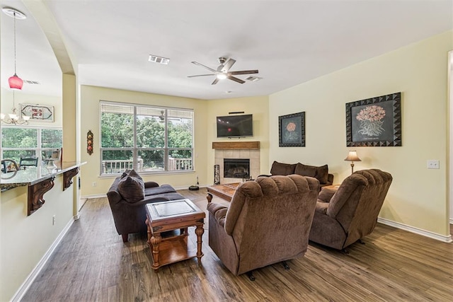 3751 Rock Dove Lndg, Edmond, OK 73034 - living room featuring dark wood finished floors, a ceiling fan, a tiled fireplace, and a chandelier