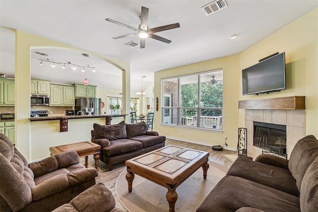 3751 Rock Dove Lndg, Edmond, OK 73034 - living room featuring light wood-type flooring, a chandelier, a tiled fireplace, and a ceiling fan