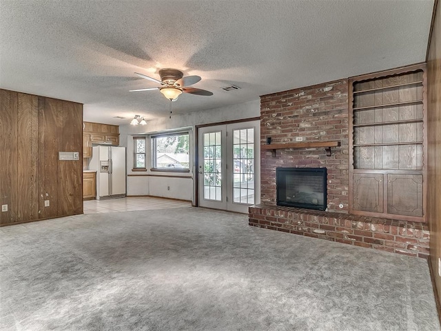 3000 Beverly Dr, Edmond, OK 73013 - unfurnished living room featuring a ceiling fan, light carpet, a textured ceiling, wooden walls, and a fireplace