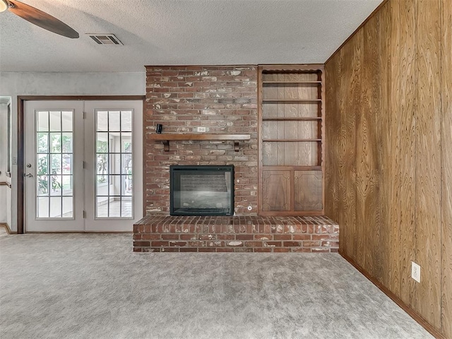 3000 Beverly Dr, Edmond, OK 73013 - unfurnished living room featuring carpet flooring, wooden walls, a textured ceiling, ceiling fan, and a brick fireplace