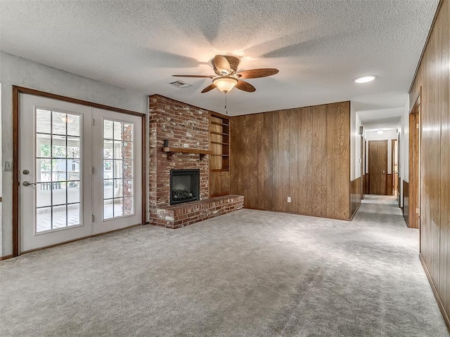 3000 Beverly Dr, Edmond, OK 73013 - unfurnished living room featuring wood walls, ceiling fan, a textured ceiling, carpet flooring, and built in shelves