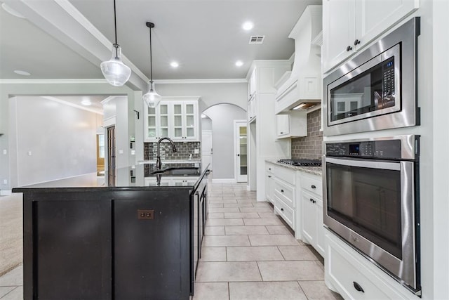 9041 NW 147th Ter, Yukon, OK 73099 - kitchen with stainless steel appliances, premium range hood, tasteful backsplash, arched walkways, and white cabinetry
