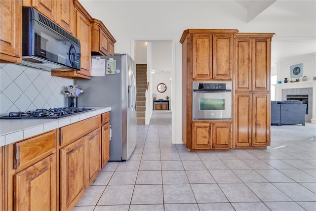 1045 Belmont Pl, Yukon, OK 73099 - kitchen featuring appliances with stainless steel finishes, tile counters, tasteful backsplash, light tile patterned floors, and brown cabinetry