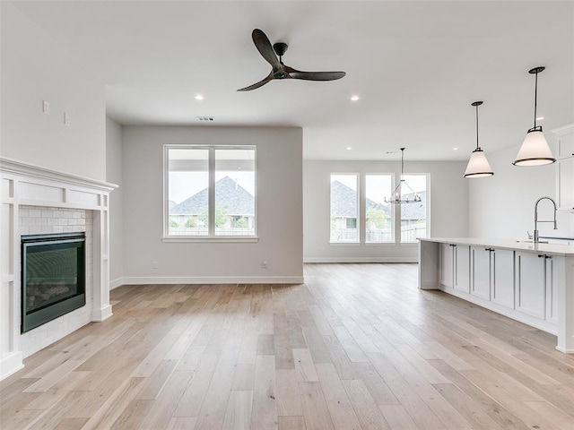 201 Pont Neuf Ct, Edmond, OK 73034 - unfurnished living room featuring light wood finished floors, a brick fireplace, a chandelier, ceiling fan, and recessed lighting