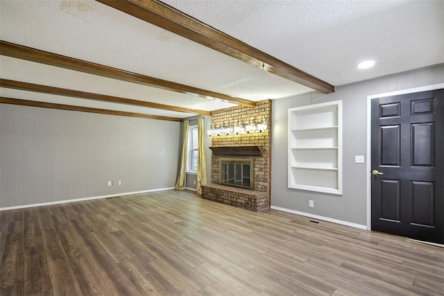 11904 Somerville Dr, Yukon, OK 73099 - unfurnished living room with a textured ceiling, beam ceiling, a fireplace, wood finished floors, and built in shelves