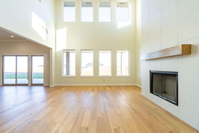 4334 White Ash Dr, Piedmont, OK 73078 - unfurnished living room featuring a tile fireplace, a high ceiling, light wood-type flooring, and plenty of natural light