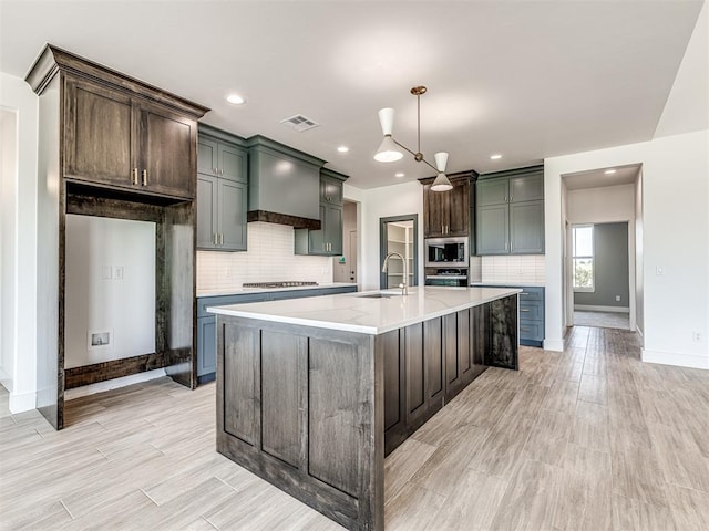 6881 Lake View Ct, Cashion, OK 73016 - kitchen featuring decorative backsplash, stainless steel microwave, light wood-style flooring, a large island with sink, and recessed lighting