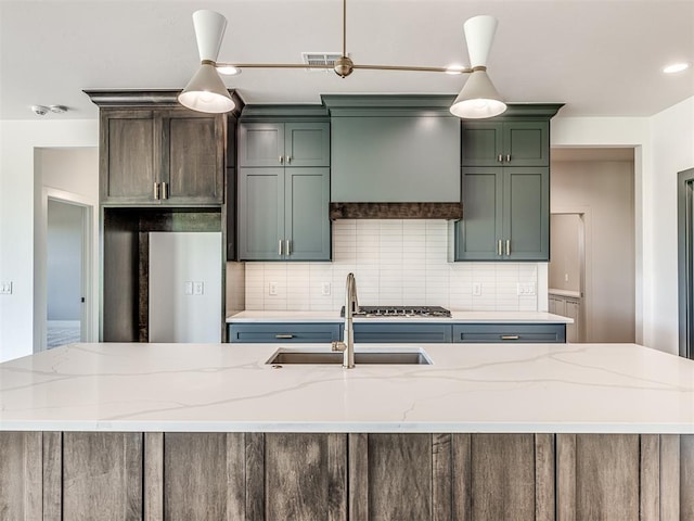 6881 Lake View Ct, Cashion, OK 73016 - kitchen with custom range hood, decorative backsplash, light stone counters, a center island with sink, and pendant lighting