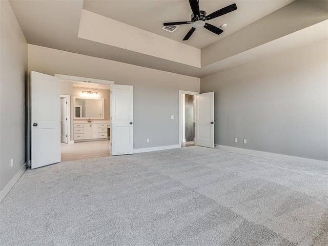 6881 Lake View Ct, Cashion, OK 73016 - unfurnished bedroom featuring light carpet, ensuite bath, a tray ceiling, and a ceiling fan