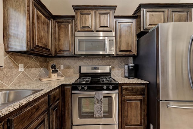 2305 Makaila Way, Yukon, OK 73099 - kitchen featuring appliances with stainless steel finishes, dark brown cabinetry, backsplash, and light stone countertops