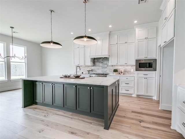 216 Pont Neuf Ct, Edmond, OK 73034 - kitchen featuring stainless steel microwave, white cabinetry, backsplash, an island with sink, and light wood finished floors