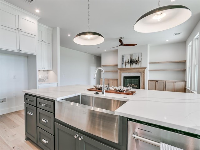 216 Pont Neuf Ct, Edmond, OK 73034 - kitchen with stainless steel dishwasher, light wood finished floors, white cabinetry, a glass covered fireplace, and hanging light fixtures