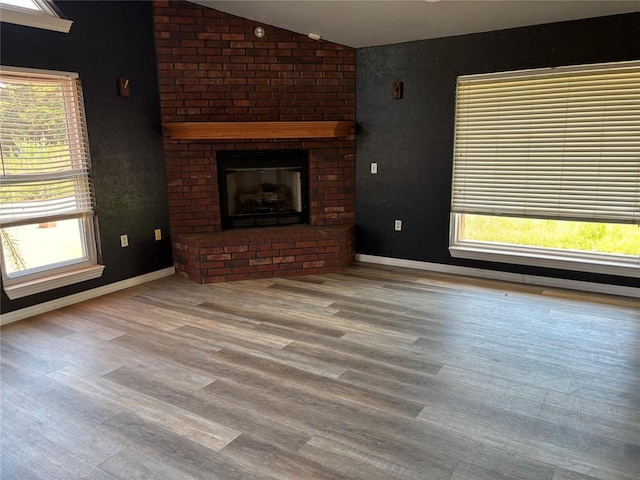 unfurnished living room with plenty of natural light, vaulted ceiling, a fireplace, and wood finished floors