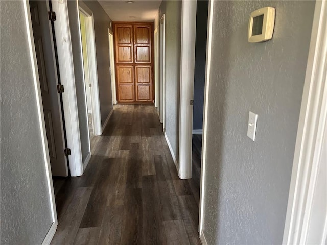 hallway featuring a textured wall and dark wood-style floors