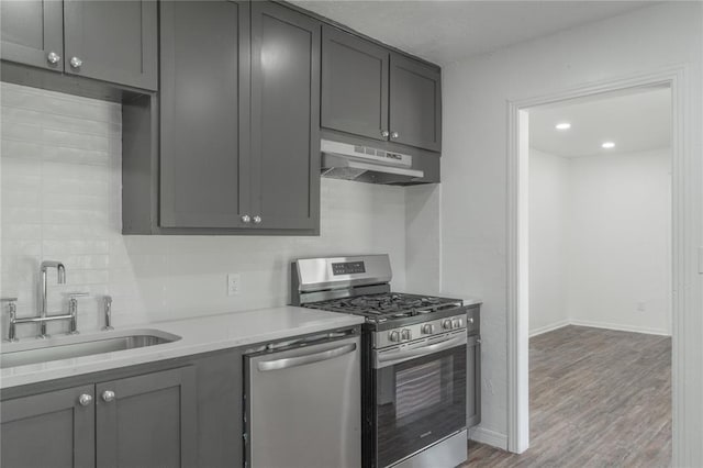 1120 SW 47th St, Oklahoma City, OK 73109 - kitchen featuring appliances with stainless steel finishes, under cabinet range hood, tasteful backsplash, gray cabinetry, and light countertops