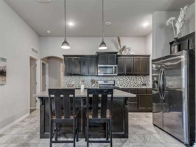 3529 Slate River Dr, Yukon, OK 73099 - kitchen with appliances with stainless steel finishes, light marble finish floors, arched walkways, light countertops, and a kitchen island with sink