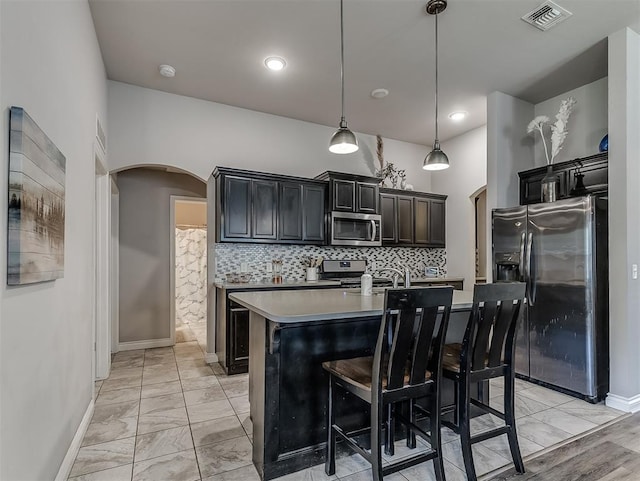3529 Slate River Dr, Yukon, OK 73099 - kitchen featuring appliances with stainless steel finishes, arched walkways, decorative backsplash, a kitchen island with sink, and light marble finish flooring