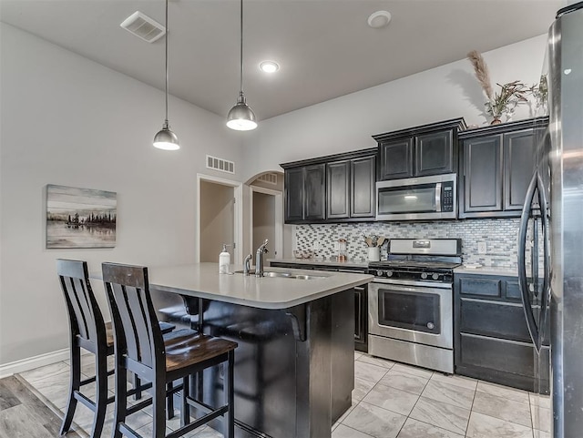 3529 Slate River Dr, Yukon, OK 73099 - kitchen featuring appliances with stainless steel finishes, light countertops, tasteful backsplash, arched walkways, and a kitchen island with sink