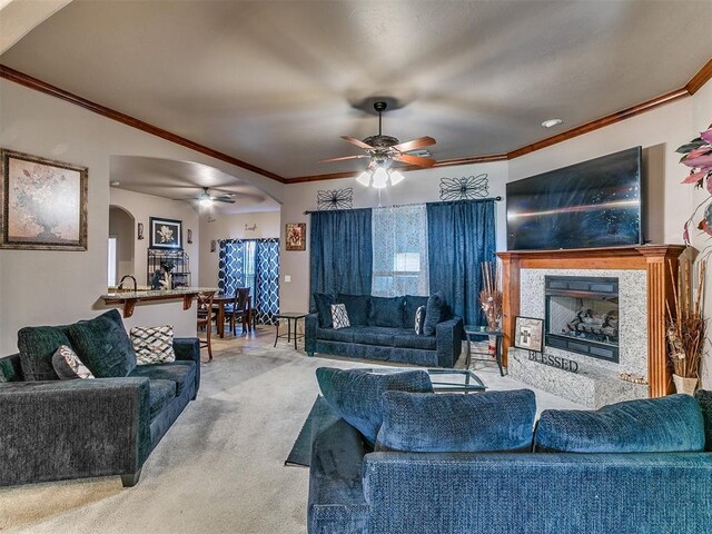 living area featuring arched walkways, ceiling fan, ornamental molding, a fireplace, and light carpet