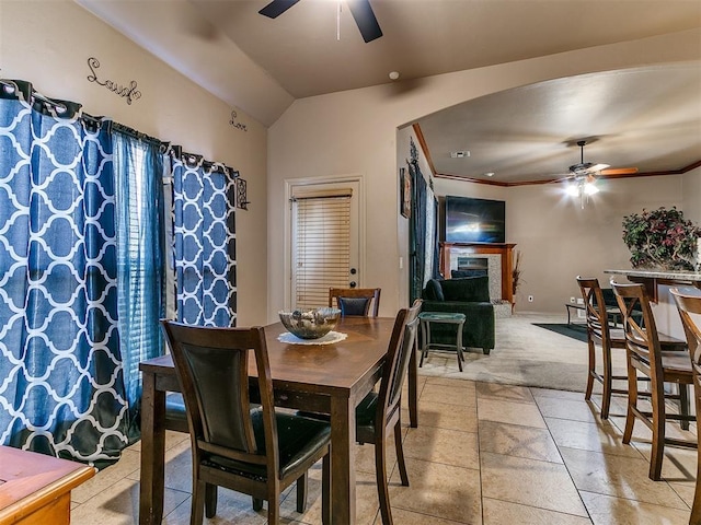 dining space with ceiling fan, arched walkways, vaulted ceiling, a fireplace, and light colored carpet