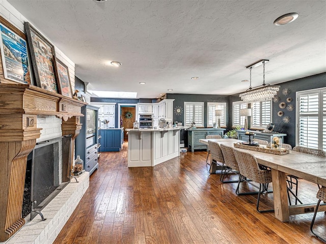 1521 Spring Creek Dr, Yukon, OK 73099 - kitchen with a brick fireplace, dark wood-type flooring, a kitchen breakfast bar, light countertops, and a textured ceiling