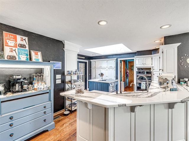 1521 Spring Creek Dr, Yukon, OK 73099 - kitchen with double oven, a peninsula, light wood-type flooring, white cabinetry, and a breakfast bar area