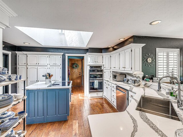 1521 Spring Creek Dr, Yukon, OK 73099 - kitchen featuring stainless steel appliances, a skylight, white cabinetry, light wood-style floors, and a kitchen island
