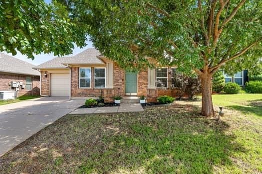 2709 NW 184th St, Edmond, OK 73012 - view of property hidden behind natural elements featuring concrete driveway, a garage, a front lawn, and brick siding