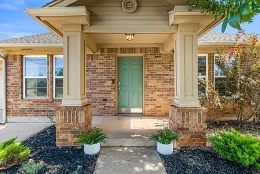 2709 NW 184th St, Edmond, OK 73012 - doorway to property featuring brick siding, a porch, and a shingled roof