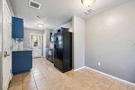 2709 NW 184th St, Edmond, OK 73012 - kitchen with black refrigerator with ice dispenser, blue cabinets, and light tile patterned floors