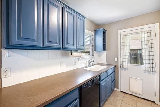 2709 NW 184th St, Edmond, OK 73012 - kitchen with blue cabinets, black dishwasher, light tile patterned floors, and open shelves