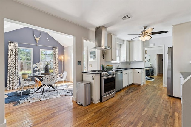 2625 Somerset Pl, Oklahoma City, OK 73116 - kitchen with wall chimney exhaust hood, appliances with stainless steel finishes, wood finished floors, white cabinetry, and a ceiling fan