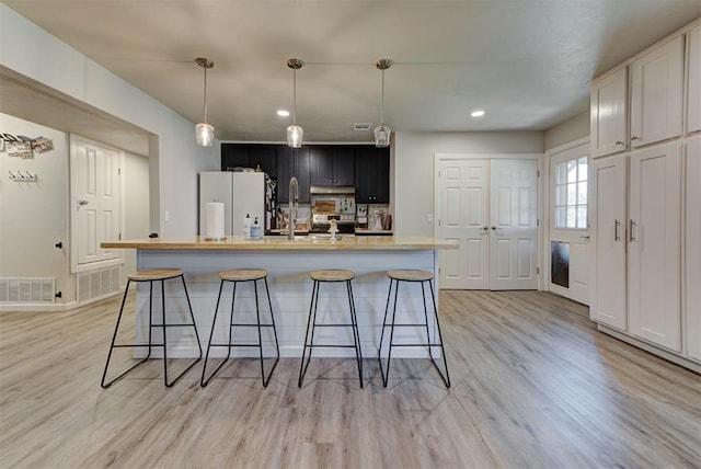 201 N English Dr, Moore, OK 73160 - kitchen featuring freestanding refrigerator, light wood-style floors, light countertops, a breakfast bar, and an island with sink