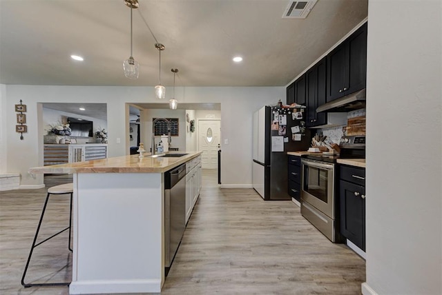 201 N English Dr, Moore, OK 73160 - kitchen with appliances with stainless steel finishes, dark cabinetry, under cabinet range hood, light wood-style flooring, and recessed lighting