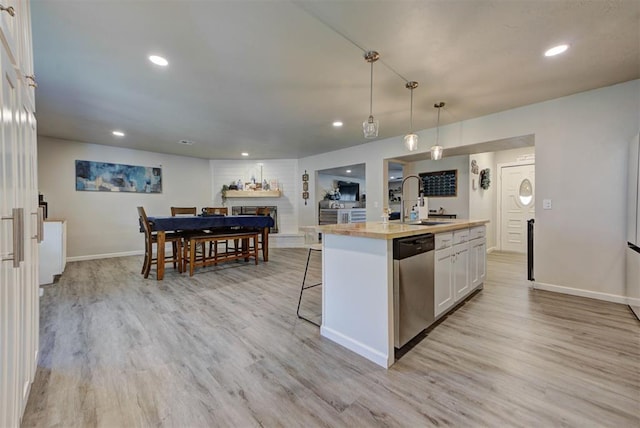 201 N English Dr, Moore, OK 73160 - kitchen featuring dishwasher, white cabinets, light wood finished floors, a fireplace with raised hearth, and a kitchen island with sink