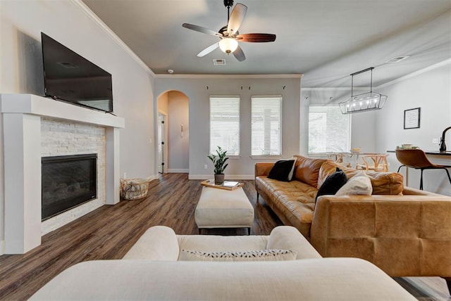 9920 NW 142nd St, Yukon, OK 73099 - living room featuring ornamental molding, wood finished floors, arched walkways, ceiling fan, and a stone fireplace
